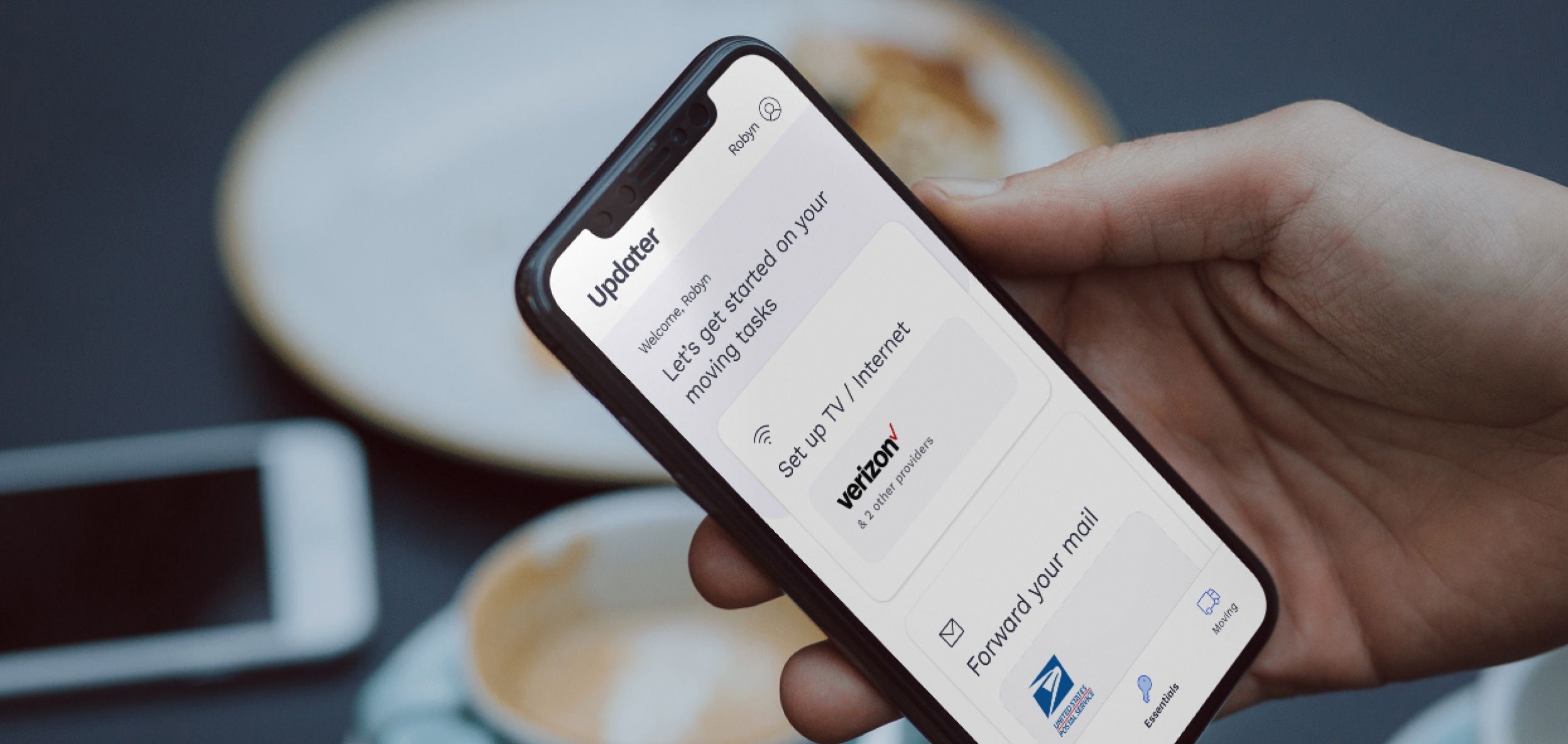 A man is using the Updater application on his phone in a coffee shop to view his moving tasks