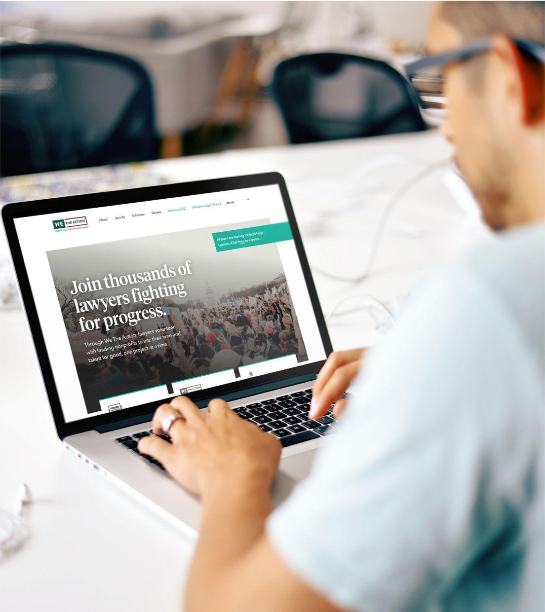 A person in an office conference room views the We the Action application homescreen on a laptop to learn how to join lawyers fighting for progress